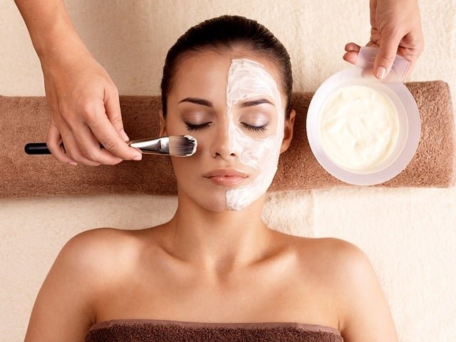 une femme se fait appliquer de la crème sur le visage avec un pinceau